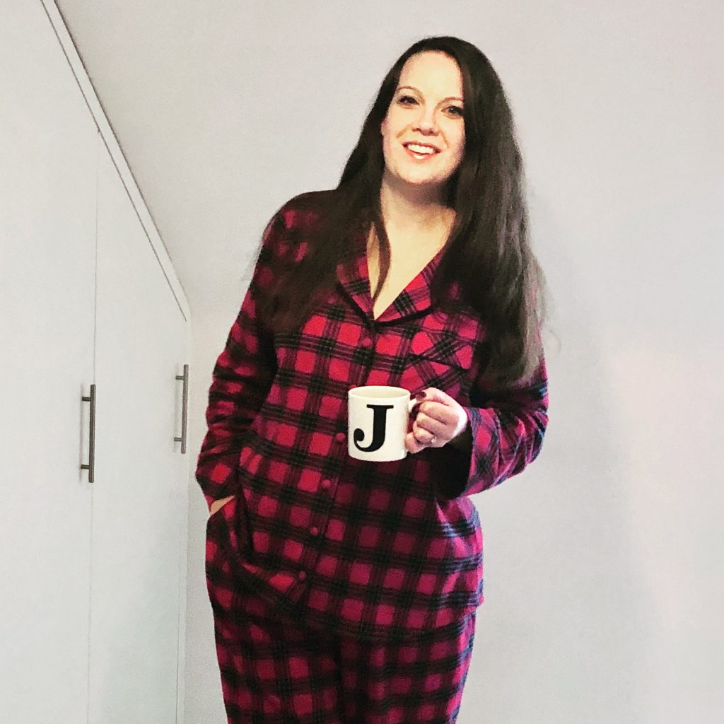 Julia in red tartan pyjamas holding a mug with a J on it
