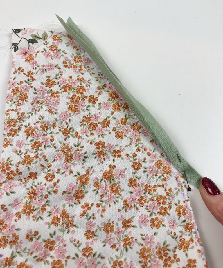 a hand holds binding attached to floral quilted fabric