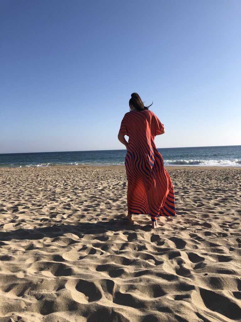 Julia in long purple and orange kaftan on a sandy beach