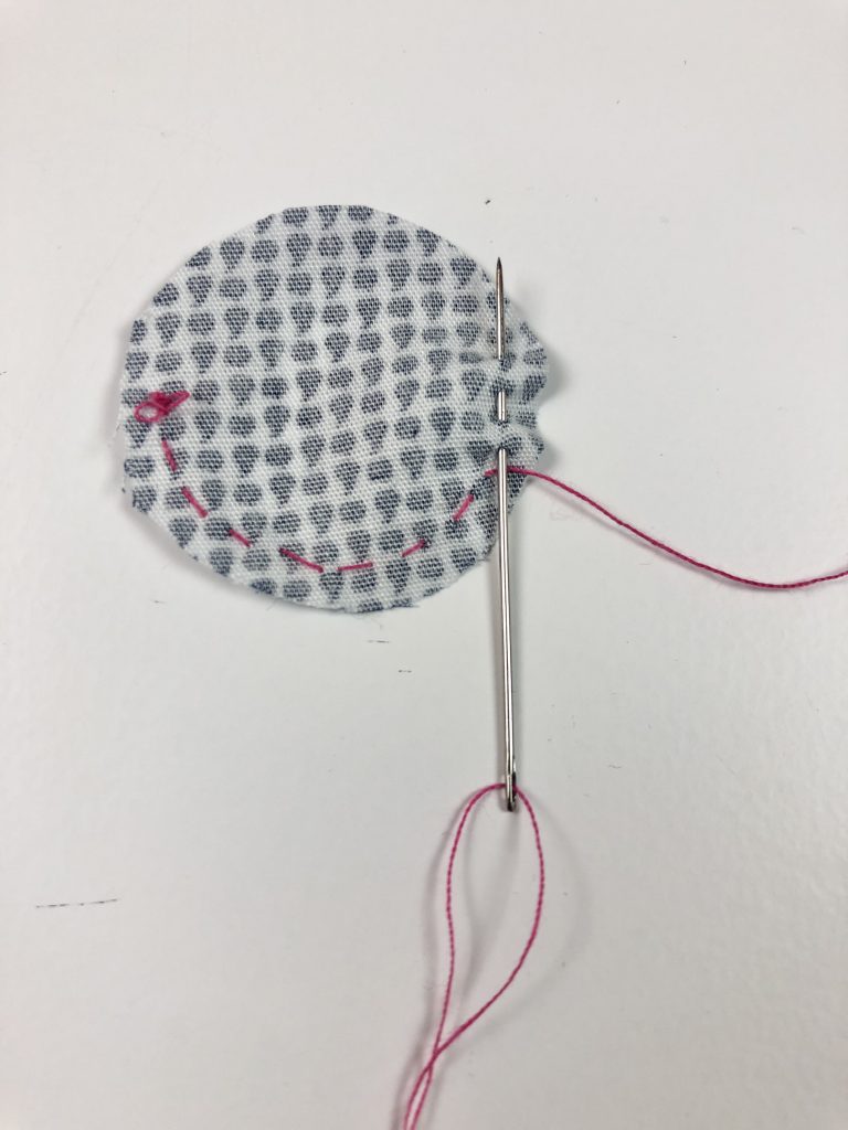 circle of fabric with small running stitches around edge