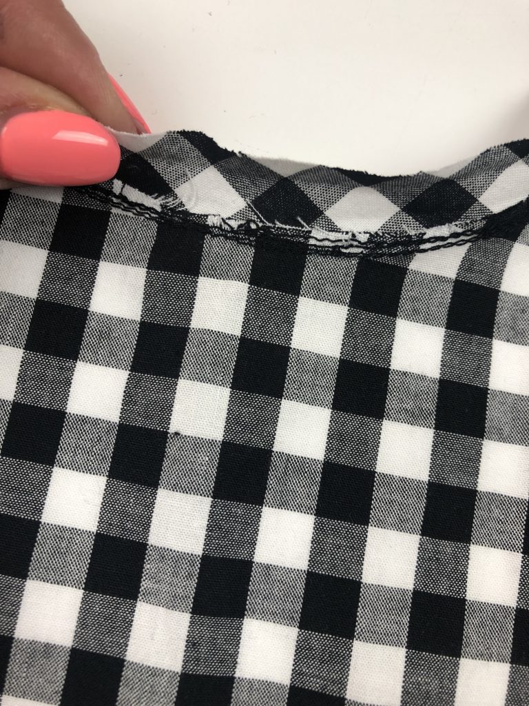 black gingham with binding attached to neckline edge. a hand is holding the binding