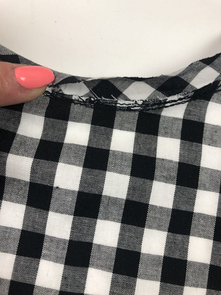 black gingham with binding attached to neckline edge. a hand is holding the binding and folding it towards the neckline