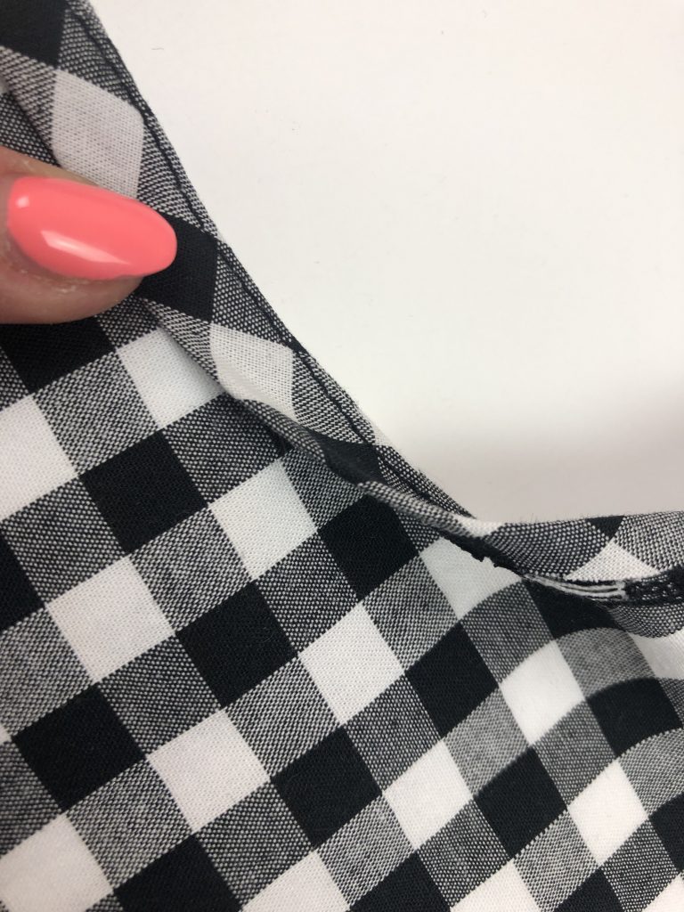 black gingham with binding attached to neckline edge. a hand is holding the binding and folding it to the inside of the garment