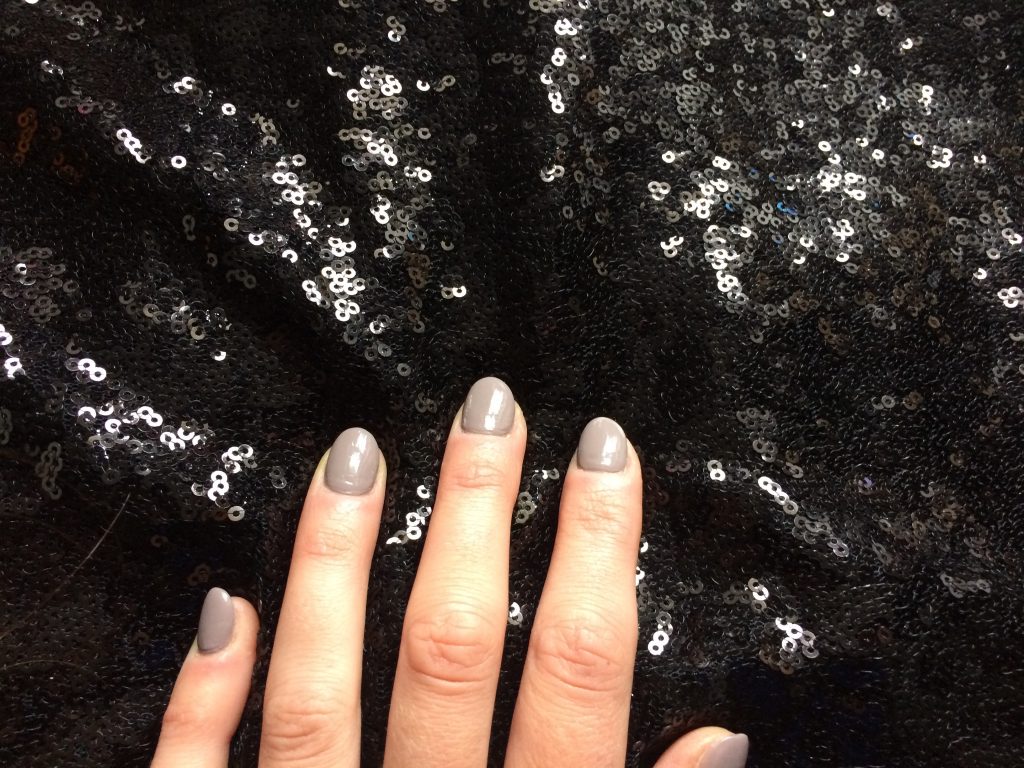 hand with grey nail varnish touching black sequin fabric
