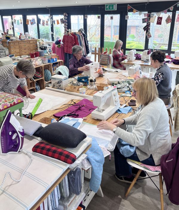 a group of women sit at a large table with their sewing machines and dressmaking projects