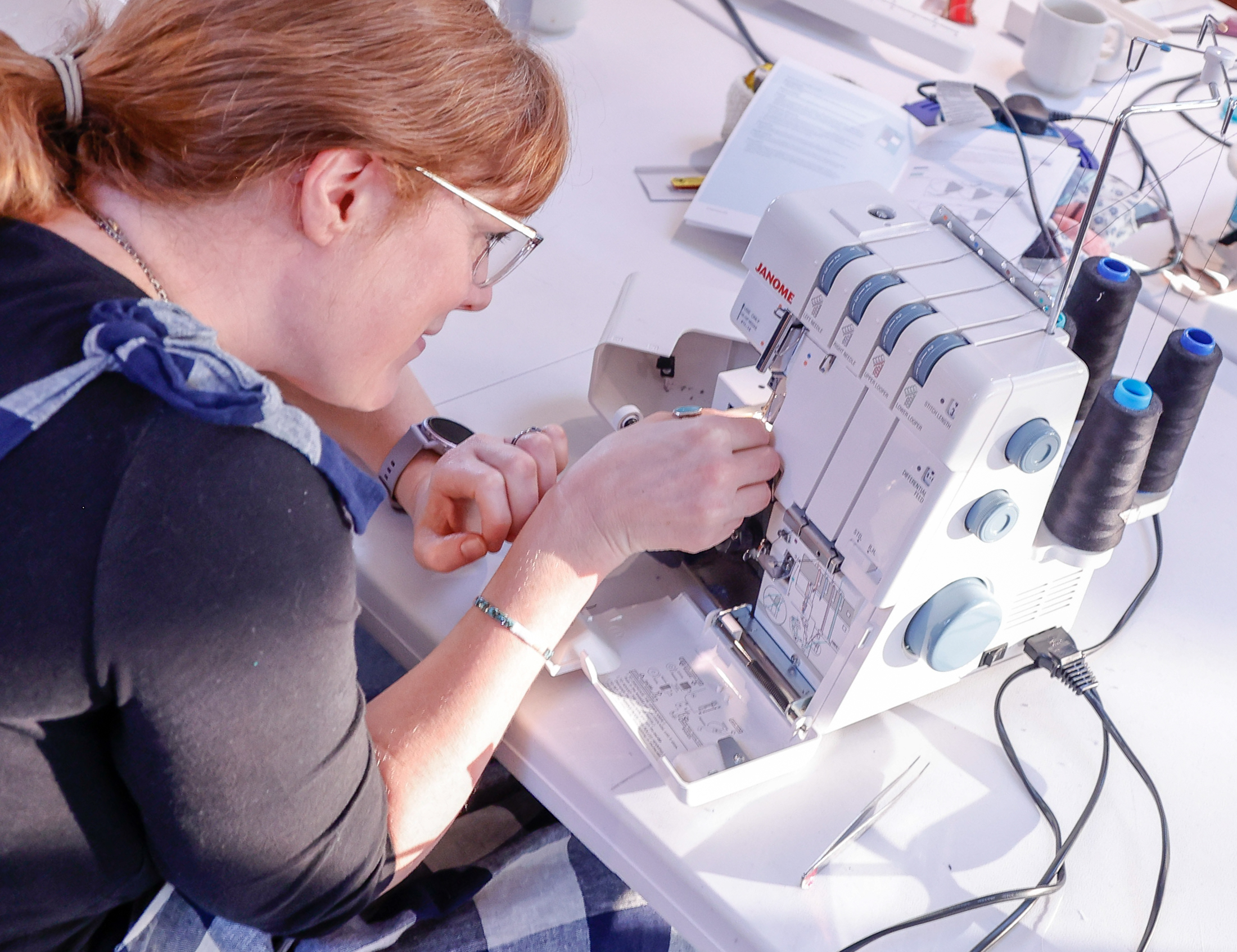 a woman is sitting next to an overlocker sewing machine trying to thread it