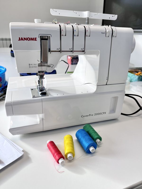White Janome coverstitch machine with red, yellow, blue and green spools of thread in front of it